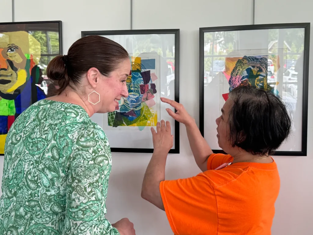 Two women smiling, discuss colorful abstract portraits at an art exhibit