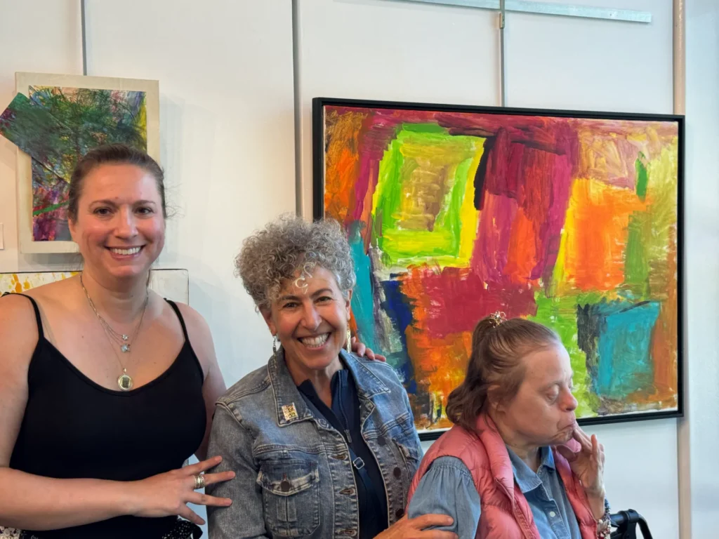 An artist and two guests smiling in front of an abstract colorful artwork